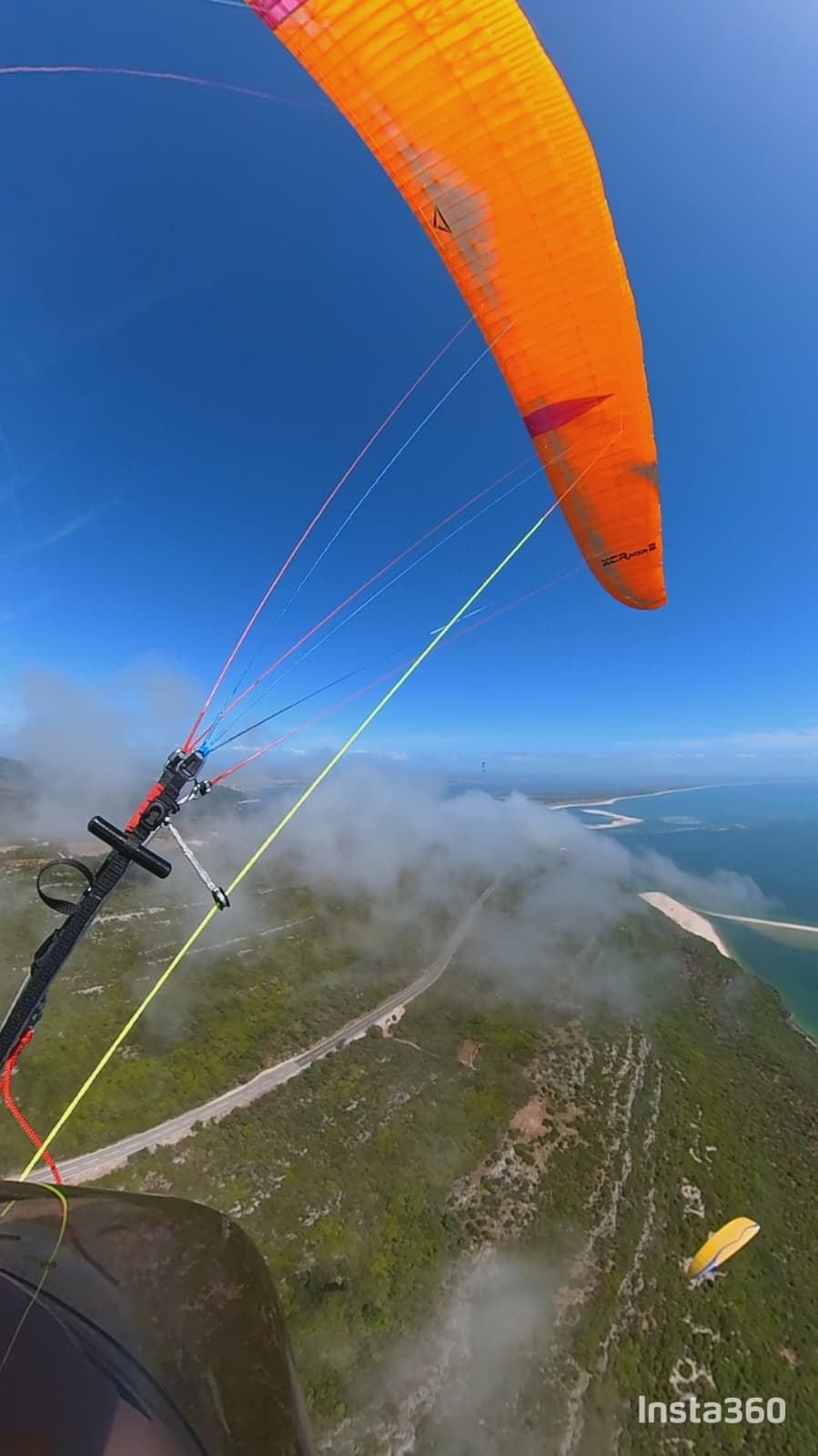 Paraglider with orange XCRacer wing soaring above the Arrábida cliffs and Atlantic coast