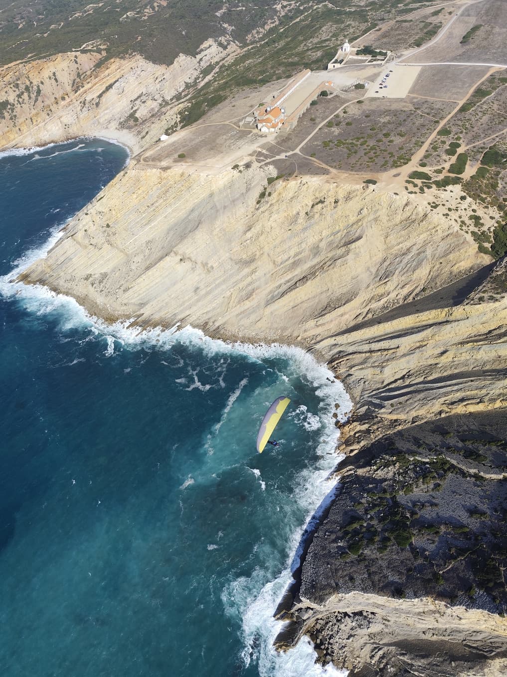 Aerial view of Cabo Espichel cliffs and chapel with paraglider above the Atlantic